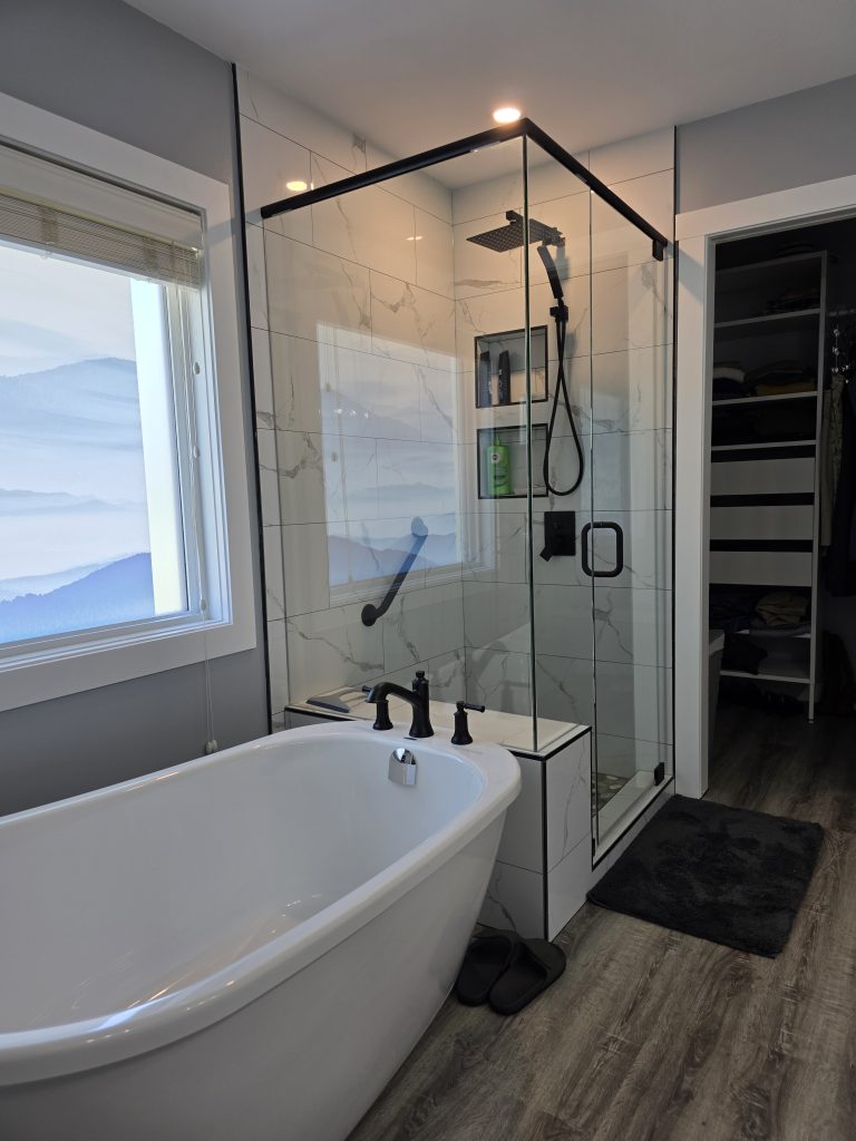 After: freestanding tub beneath the window beside a glass shower with black fixtures