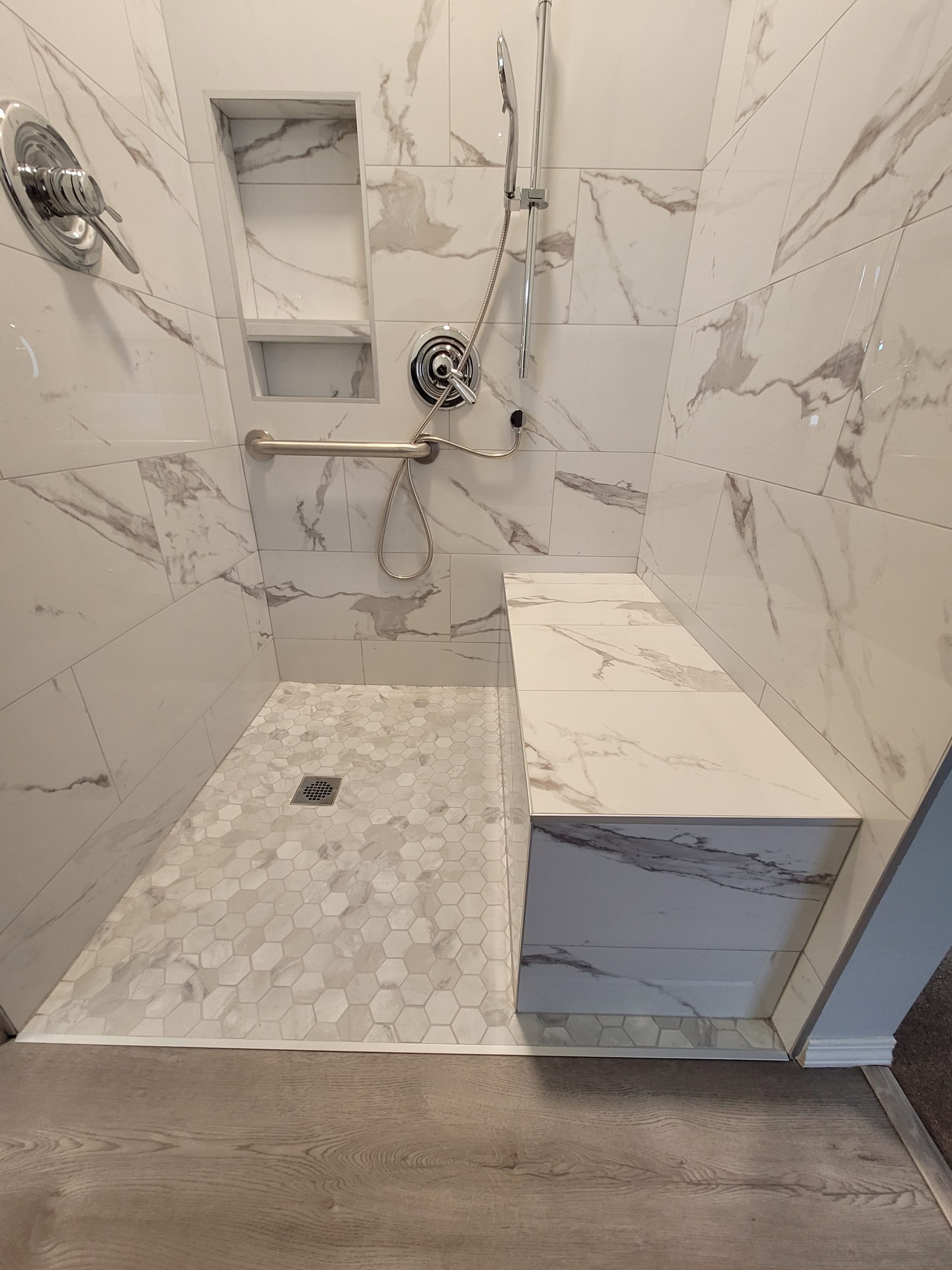 Accessible walk-in shower with low-entry floor, built-in bench, grab bar and handheld controls